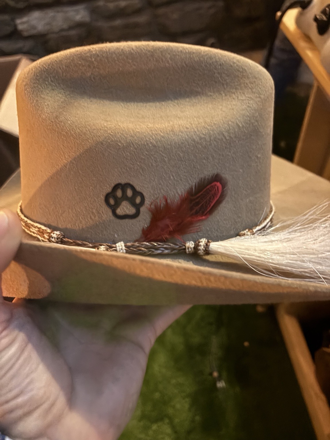 Custom felt hat with a paw-print brand, decorative band, and red and white feathers